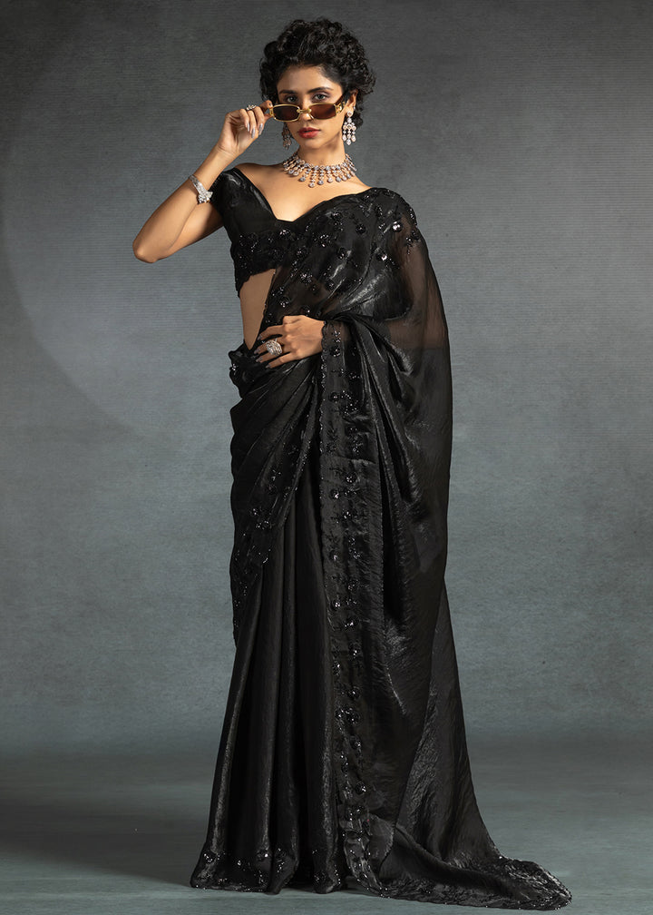 Gleaming Black satin silk saree with intricate handwork, sequins, cutwork & zarkan embroidery. Includes matching blouse piece. Perfect for wedding parties.