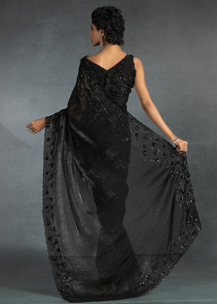 Gleaming Black satin silk saree with intricate handwork, sequins, cutwork & zarkan embroidery. Includes matching blouse piece. Perfect for wedding parties.