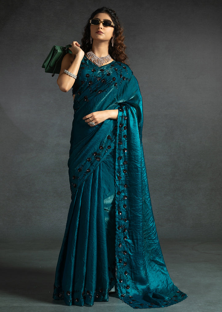 Gleaming Teal satin silk saree with intricate handwork, sequins, cutwork & zarkan embroidery. Includes matching blouse piece. Perfect for wedding parties.