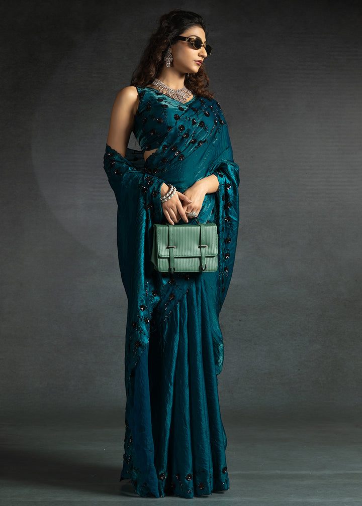 Gleaming Teal satin silk saree with intricate handwork, sequins, cutwork & zarkan embroidery. Includes matching blouse piece. Perfect for wedding parties.